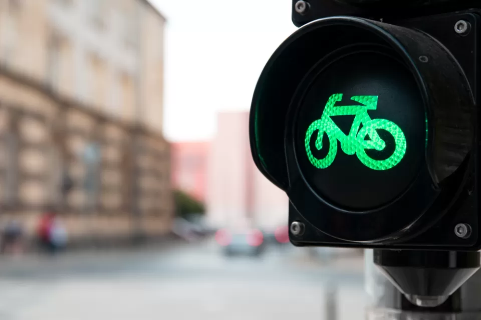 Close-up of black traffic light with green bike symbol lit up and blurry urban scene in background